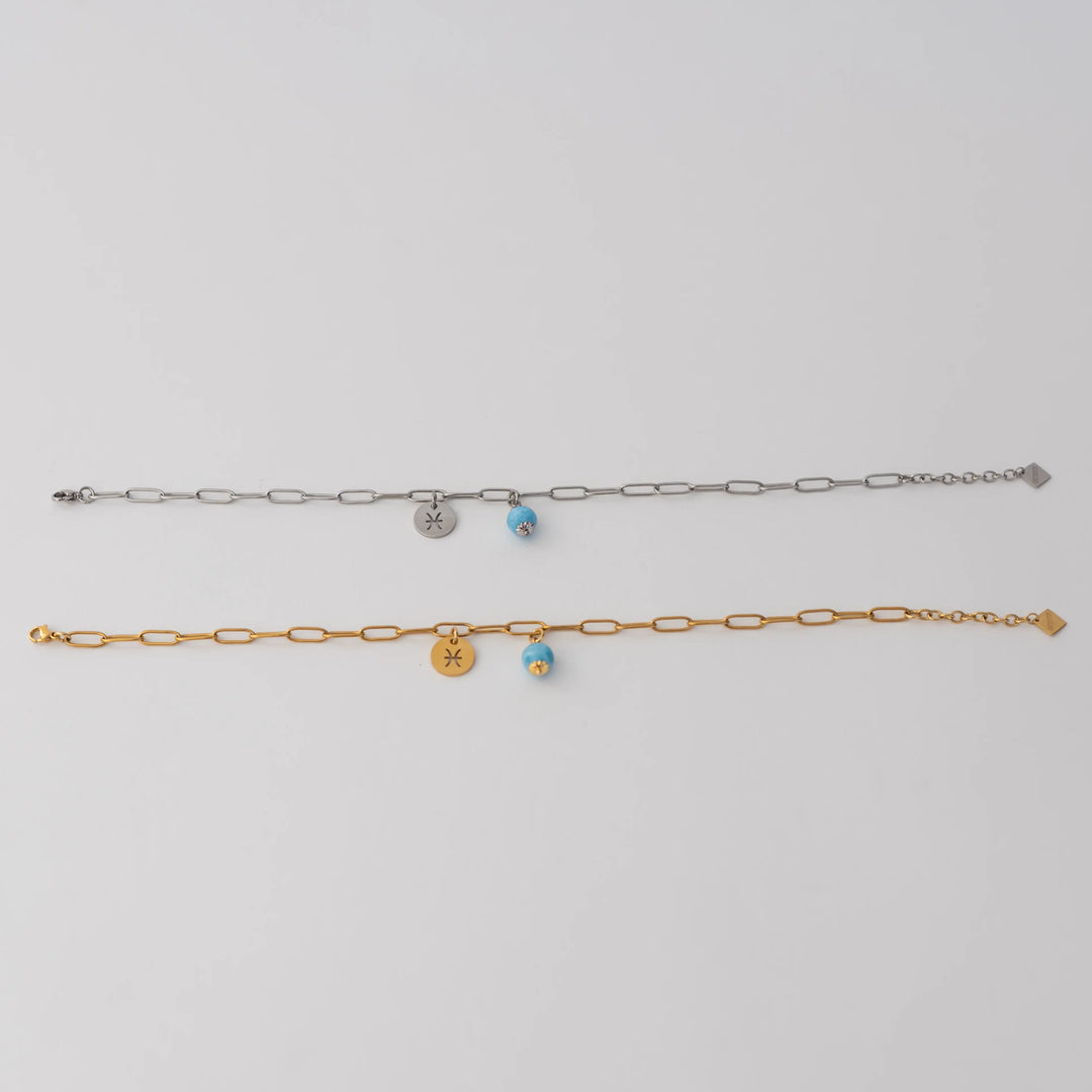 Bracelet de cheville en acier inoxydable 316L de couleur dorée ou de couleur argentée. Une perle de larimar et une breloque ronde avec un signe astrologique sont attachés à la chaine via un anneau.