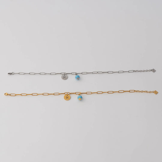 Bracelet de cheville en acier inoxydable 316L de couleur dorée ou de couleur argentée. Une perle de larimar et une breloque ronde avec un signe astrologique sont attachés à la chaine via un anneau.
