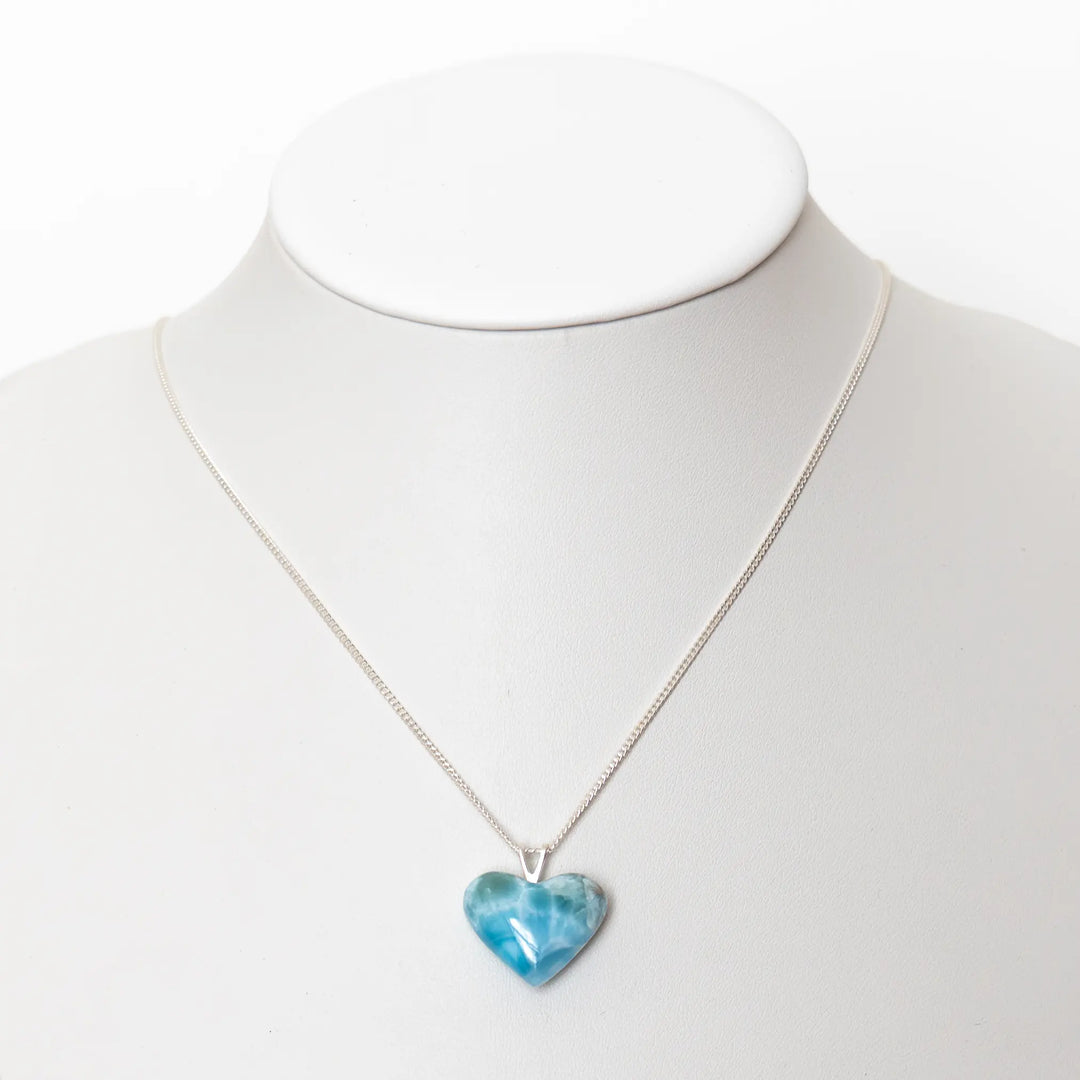Magnifique cœur en Larimar de couleur bleue monté en pendentif sur une chaîne en argent 925. Bijou présenté sur un bustier blanc.