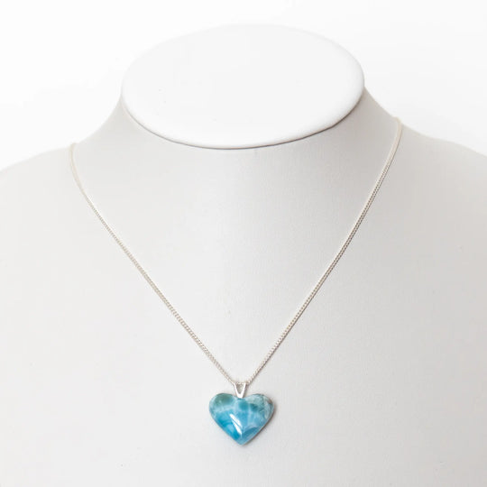 Magnifique cœur en Larimar de couleur bleue monté en pendentif sur une chaîne en argent 925. Bijou présenté sur un bustier blanc.