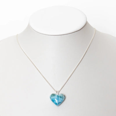 Magnifique cœur en Larimar de couleur bleue monté en pendentif sur une chaîne en argent 925. Bijou présenté sur un bustier blanc.