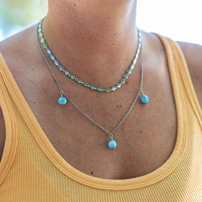 Femme portant un débardeur jaune dont on ne voit que le cou et les épaules sur la photo, portant un collier couleur argent en acier inoxydable 316L avec deux chaînes différentes. Sur la chaîne la plus longues se trouve trois perles de larimar bleue réparties à intervalle régulier.