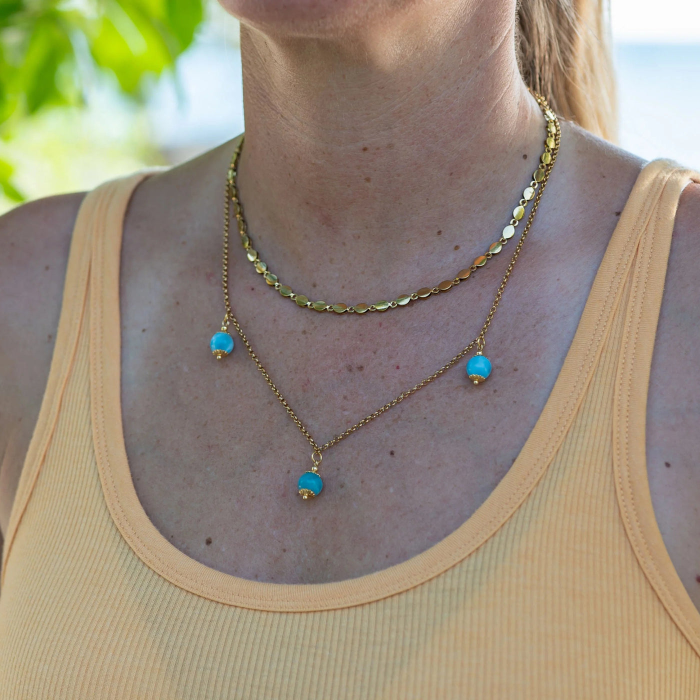 Collier en acier inoxydable 316L couleur or composé de deux chaînes différentes reliées entrent elles au niveau du fermoir. Il y a trois perles de larimar bleue sur la chaîne la plus longue.