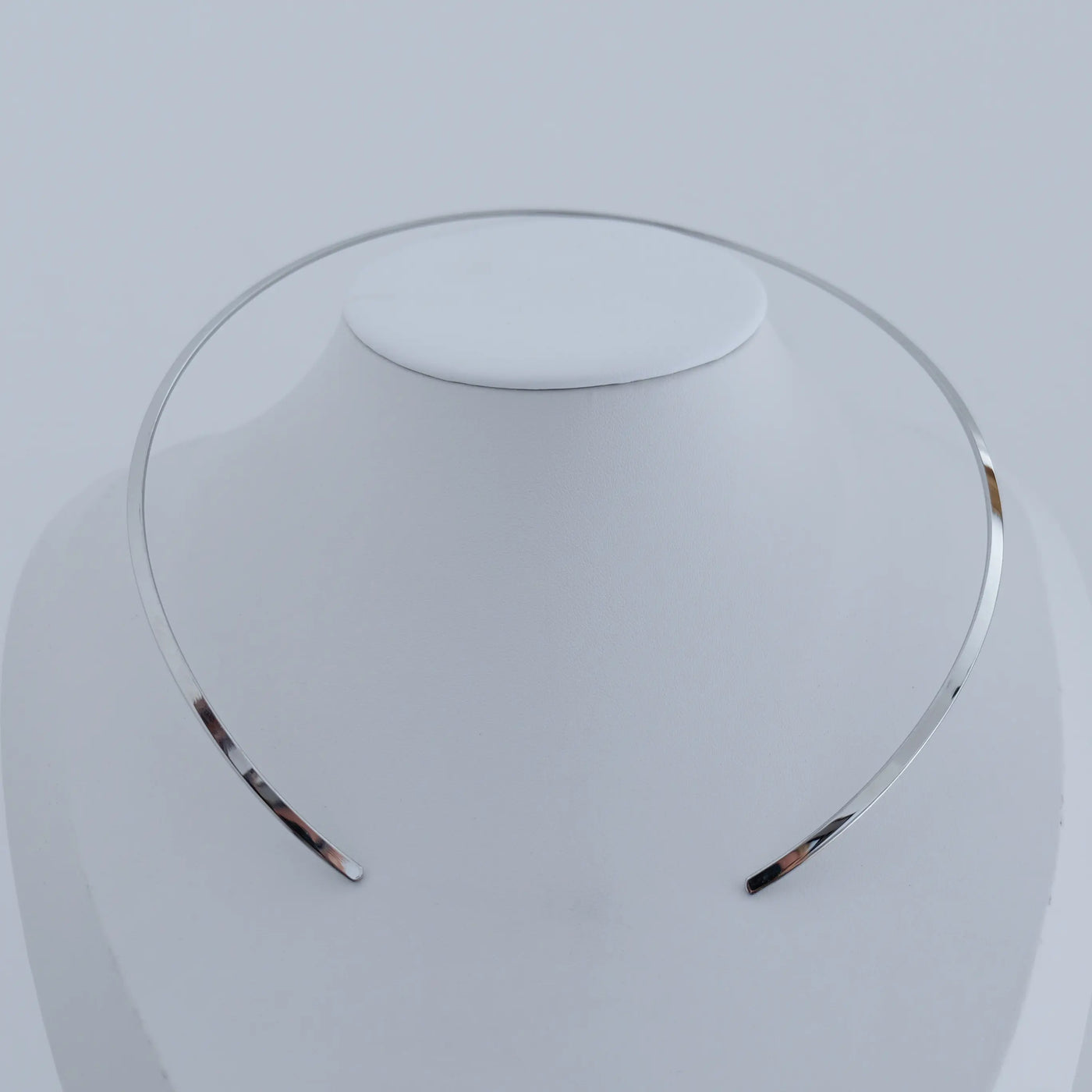 Collier rigide ouvert fait en acier inoxydable 316L présenté sur un buste blanc.