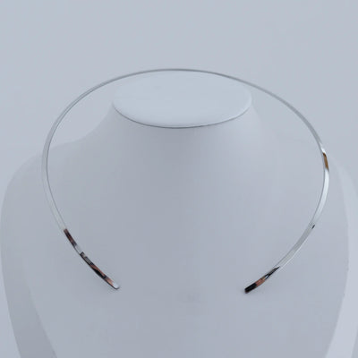 Collier rigide ouvert fait en acier inoxydable 316L présenté sur un buste blanc.