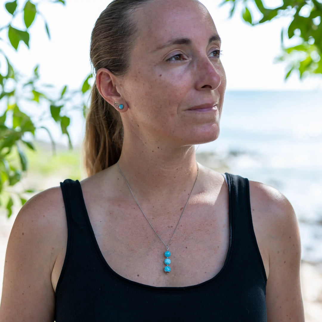 Femme prise de face regardant sur le coté et portant un collier avec trois perles de larimar de couleur bleu montées sur une chaîne argentée en acier inoxydable.