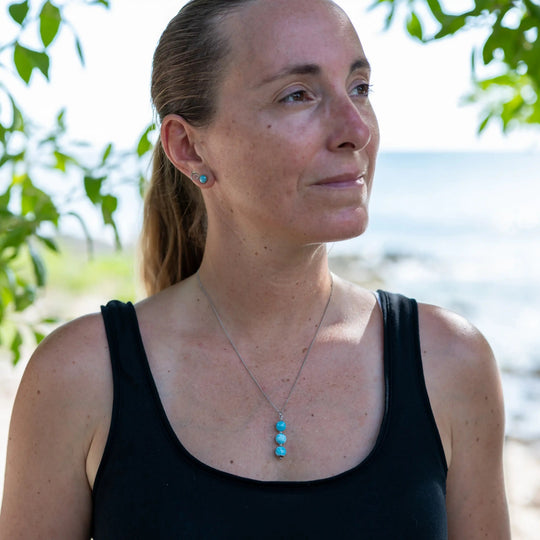 Femme prise de face regardant sur le coté et portant un collier avec trois perles de larimar de couleur bleu montées sur une chaîne argentée en acier inoxydable.