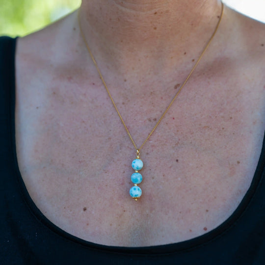 Trois perles de larimar de République Dominicaine montées sur une chaîne dorée en acier inoxydable 316L. Collier porté par une femme, seul le collier et le cou de la femme sont visibles.