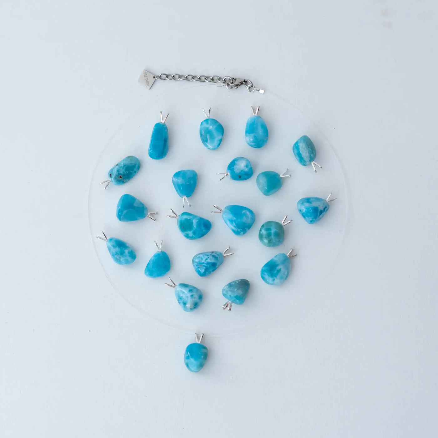 Collier fait avec un fil de pêche et un extension de chaine en acier inoxydable 316L. De nombreux cabochons de Larimar d'environ 2 centimètres de long son posés sir un fond blanc et montés sur une attache en argent 925. Chaque cabochon est taillé à la main en République Dominicaine.