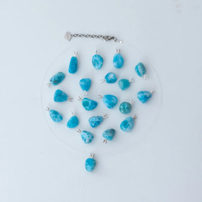 Collier fait avec un fil de pêche et un extension de chaine en acier inoxydable 316L. De nombreux cabochons de Larimar d'environ 2 centimètres de long son posés sir un fond blanc et montés sur une attache en argent 925. Chaque cabochon est taillé à la main en République Dominicaine.