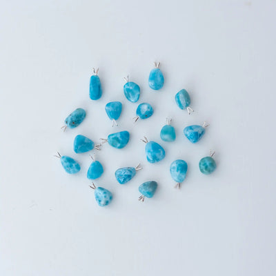 dix-neuf cabochons différents en terme de taille et de couleur, tous fait en Larimar, son posés sur un fond blanc et vue de dessus. Ces cabochons font environ deux centimètres de longueur et peuvent être montés en collier.