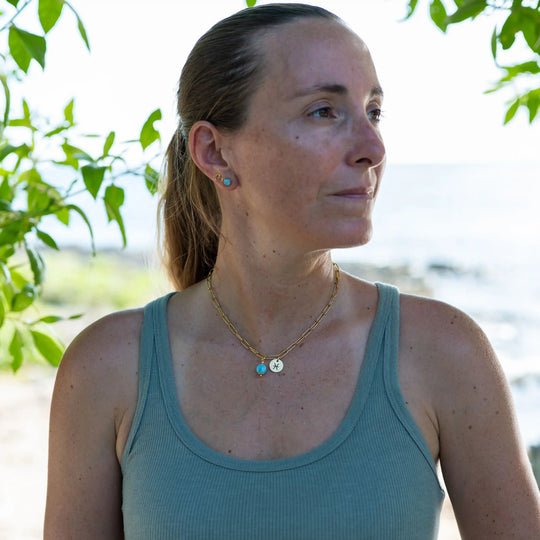 Femme vue de face avec la tête tournée sur le coté, portant un collier en acier inoxydable 316L doré, avec des mailles larges, une breloque avec un signe astrologique et une perle de Larimar.