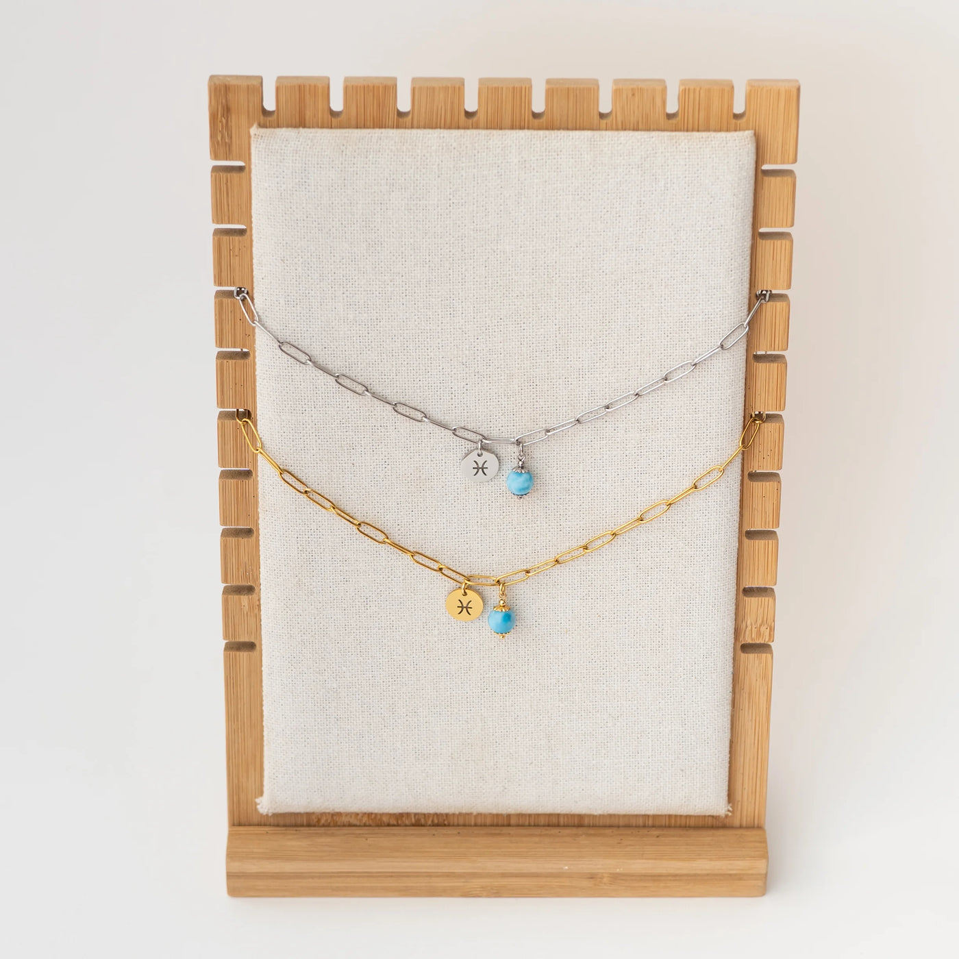 Photo de deux colliers avec des mailles larges, suspendu sur un présentoir, l'un des bracelet est en acier inoxydable 316L argenté et l'autre est en acier inoxydable doré. Une perle de larimar et un signe astrologique son attachés à la chaineen son milieu.