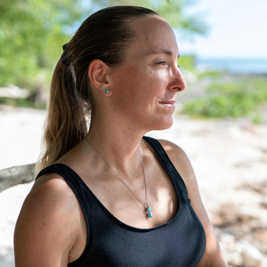 Femme vue de coté portant un collier argenté en acier inoxydable 316L avec deux perles taillées dans de la pierre naturelle de larimar de République Dominicaine.
