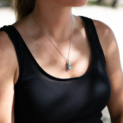 Photo d'un collier en acier inoxydable 316L ce couleur argentée avec deux perles de larimar bleu montées sur une tige en acier inoxydable.