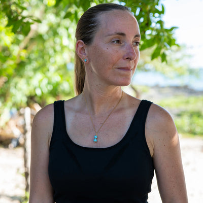photo d'une femme vue de face avec un top noir et un collier en acier inoxydable couleur argent sur lequel est montée un pendant avec deux perles de larimar de couleur bleu.