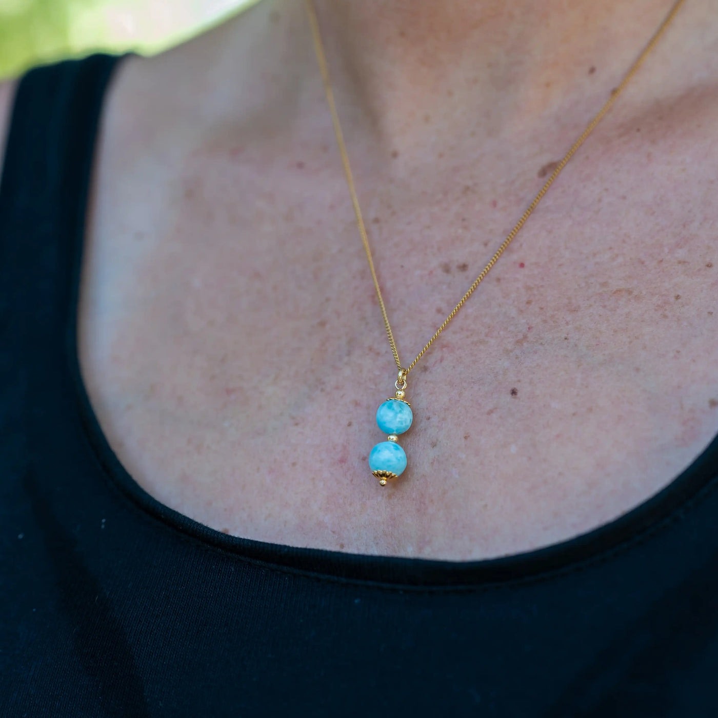 Photo en gros plan d'un collier en acier inoxydable 316L de couleur dorée sur lequel est monté un pendant avec deux perles de larimar de République Dominicaine. Seul la partie avec les deux pierres naturelles de larimar est net, le reste de la photo est flou