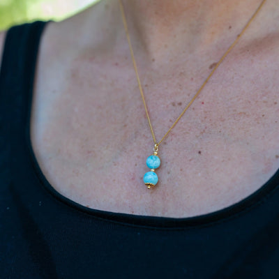 Photo en gros plan d'un collier en acier inoxydable 316L de couleur dorée sur lequel est monté un pendant avec deux perles de larimar de République Dominicaine. Seul la partie avec les deux pierres naturelles de larimar est net, le reste de la photo est flou