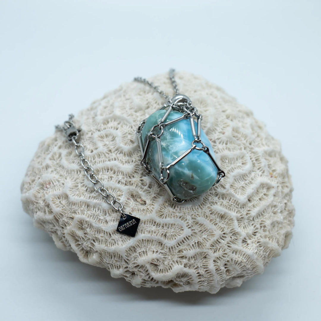Pierre naturelle de Larimar polie, de couleur bleue, contenue dans une cage en acier inoxydable et portée en collier. Larimar de République Dominicaine.