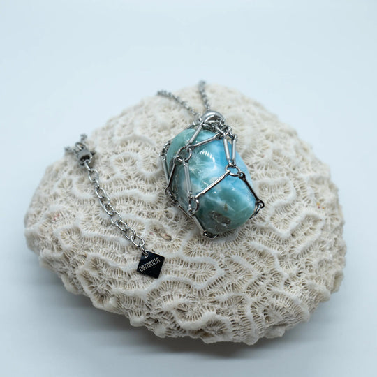 Pierre naturelle de Larimar polie, de couleur bleue, contenue dans une cage en acier inoxydable et portée en collier. Larimar de République Dominicaine.