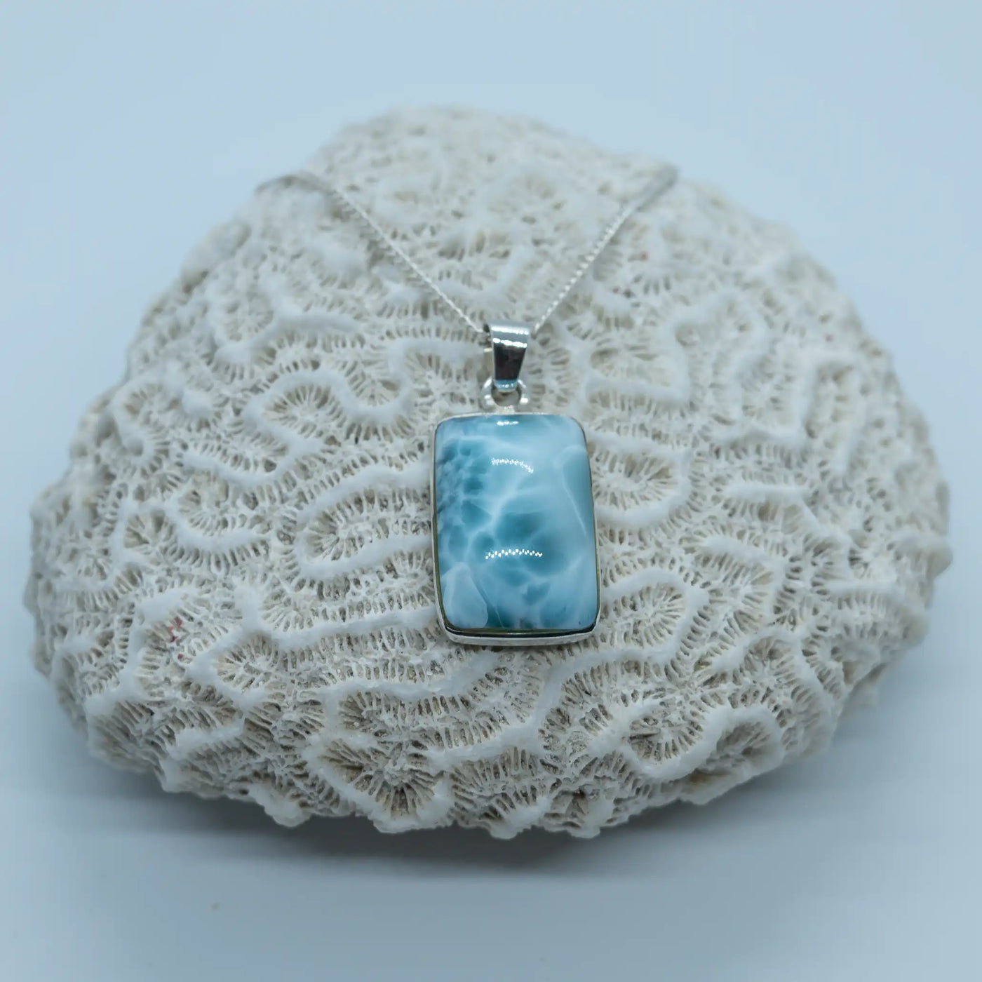 Cabochon rectangulaire en Larimar vue de face. Collier posé sur un coquillage blanc de type corail. Pierre naturelle bleu de qualité exceptionnelle.