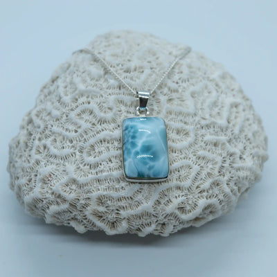 Cabochon rectangulaire en Larimar vue de face. Collier posé sur un coquillage blanc de type corail. Pierre naturelle bleu de qualité exceptionnelle.