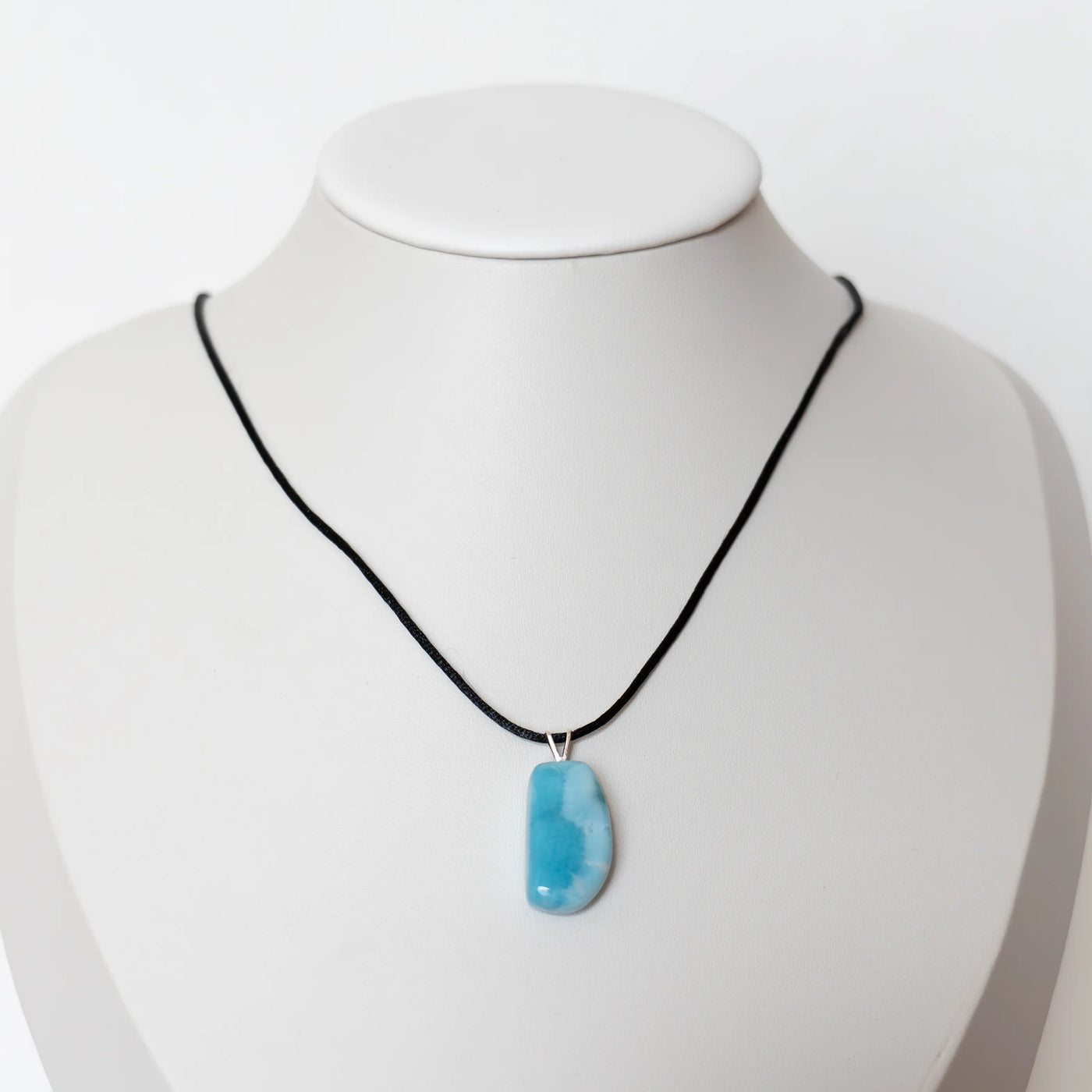 Collier en cordon noir avec un pendentif en pierre de Larimar de République Dominicaine. Bijou posé sur un présentoir en forme de buste.