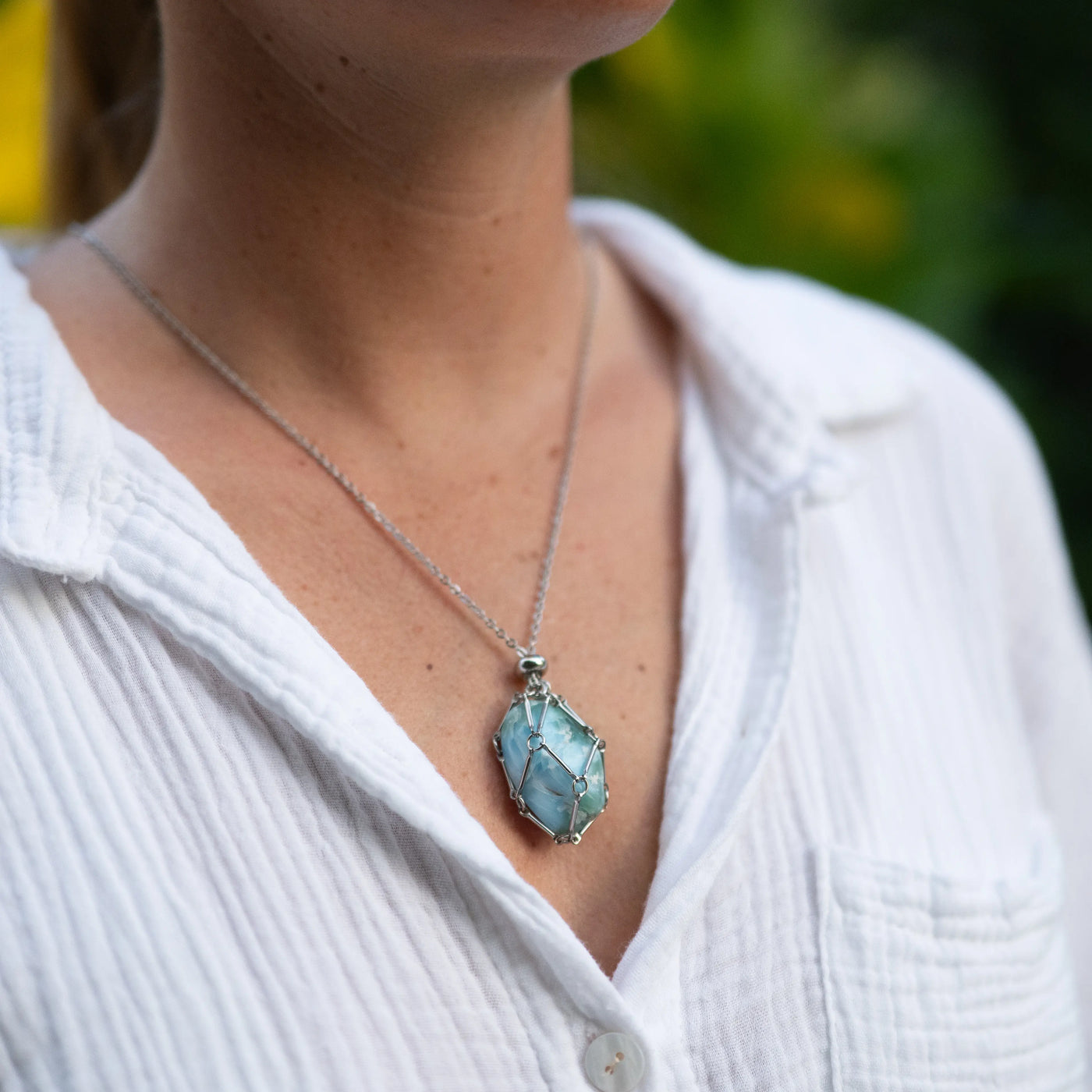 Collier en acier inoxydable argenté 316L avec une petite cage ouvrable contenant une pierre naturelle de Larimar polie de couleur bleue. Bijou porté par une femme. Bijou Larimar. 