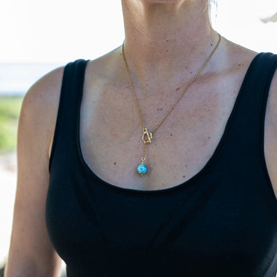 Photo d'une perle de larimar bleue portée en collier en acier chirurgical 316L couleur or avec attache sur le devant. 