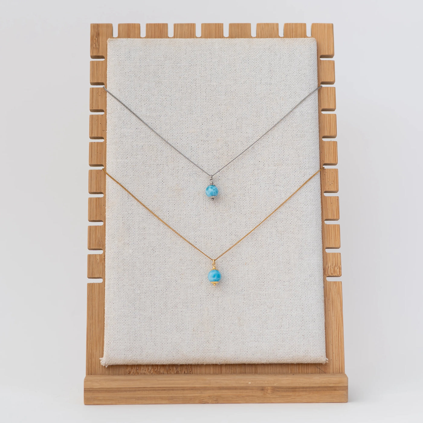 Présentoir avec un collier en acier inoxydable 316L argenté et un collier en acier inoxydable 316L doré. Chaque collier possède une perle de larimar en pendant.