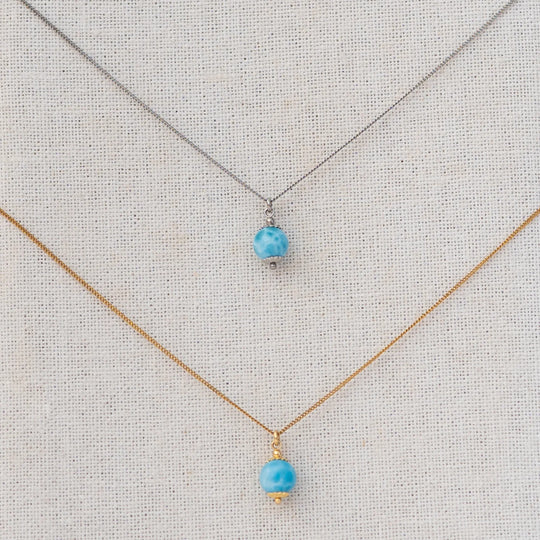 Vue serrée sur deux perles de larimar étant chacune reliées à une chaine en acier inoxydable via un anneau.