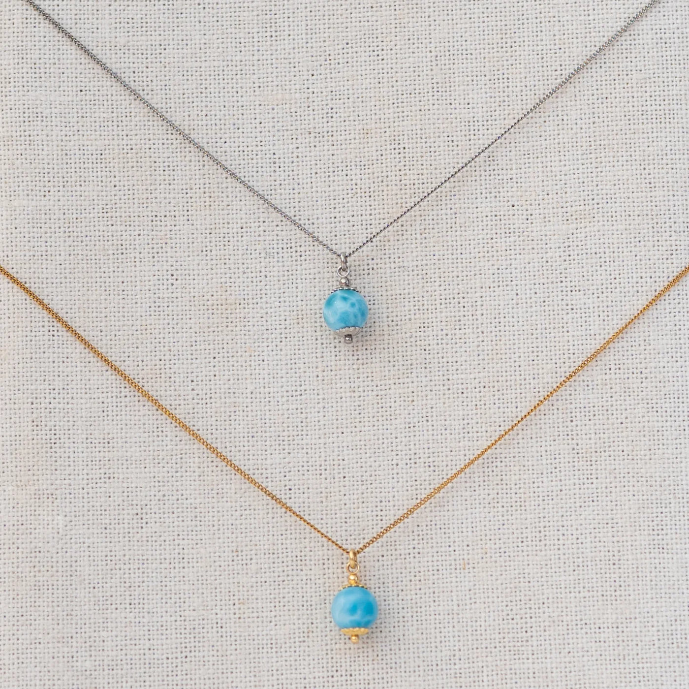 Vue serrée sur deux perles de larimar étant chacune reliées à une chaine en acier inoxydable via un anneau.