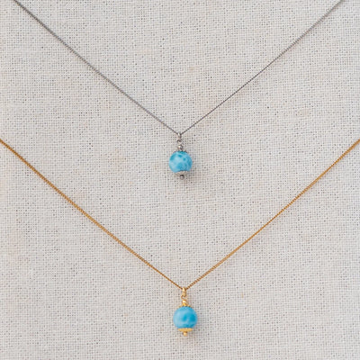 Vue serrée sur deux perles de larimar étant chacune reliées à une chaine en acier inoxydable via un anneau.