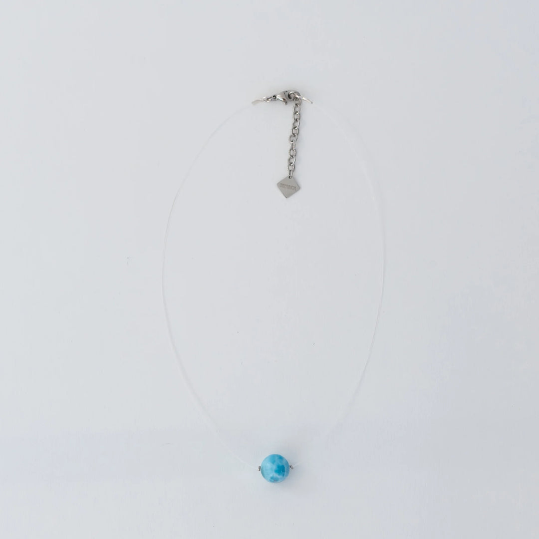 Collier raz de cou avec sa pierre de larimar de couleur bleue traversée par un fil de pêche presque invisible. Le fermoir du collier est en argent 925 et une extenttion de chaine avec une breloque orparima complète ce raz de cou.