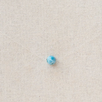 Perle de larimar origine République Dominicaine traversée par un fil de pêche pour former un collier raz de cou. Le fil est presque invisible et seule la pierre de larimar bleue ressort sur la photo.