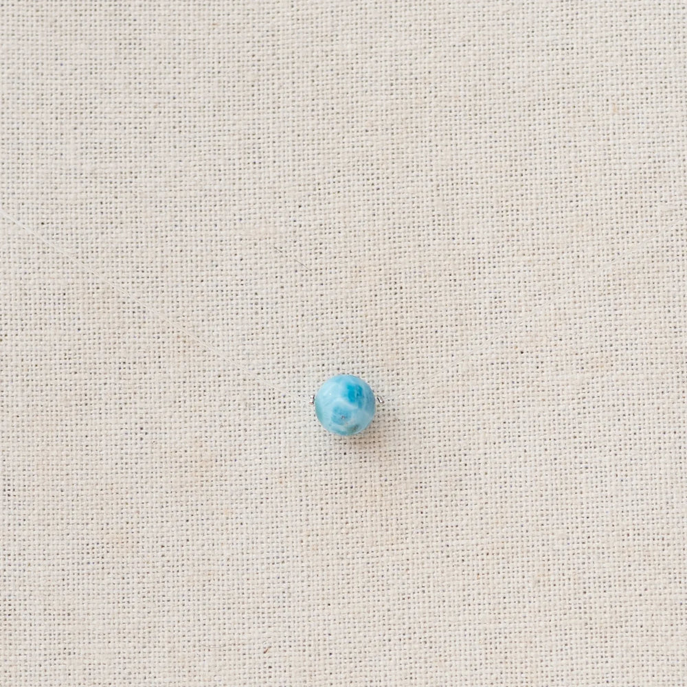 Perle de larimar origine République Dominicaine traversée par un fil de pêche pour former un collier raz de cou. Le fil est presque invisible et seule la pierre de larimar bleue ressort sur la photo.