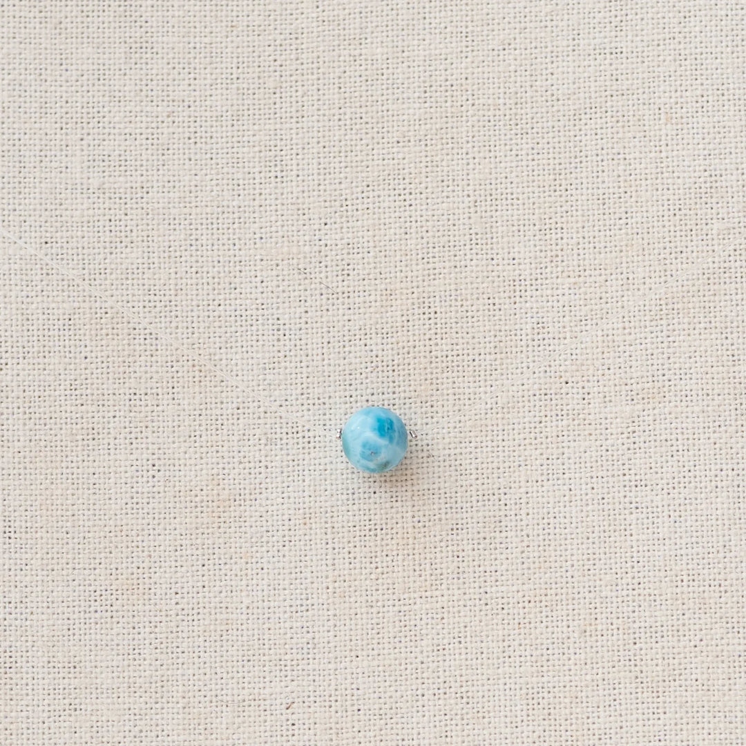 Perle de larimar origine République Dominicaine traversée par un fil de pêche pour former un collier raz de cou. Le fil est presque invisible et seule la pierre de larimar bleue ressort sur la photo.