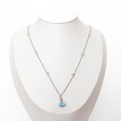Collier avec une chaîne en acier inoxydable 316 de couleur argentée posé sur un présentoir en forme de buste. Ce collier à un pendentif en pierre de Larimar de République Dominicaine. La chaîne possède plusieurs petits cœurs. Bijou fait à la main.