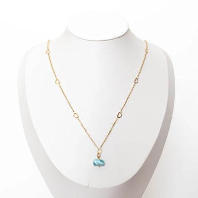 Collier en acier inoxydable 316L de couleur dorée sur laquelle se trouve un pendentif en pierre naturelle de Larimar venant de République Dominicaine. Collier posé sur un présentoir bustier.