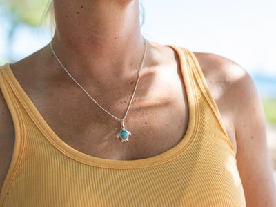 Collier en forme de tortue avec une pierre ovale en Larimar de République Dominicaine, fait en argent 925 et porté par une femme avec un débardeur jaune.