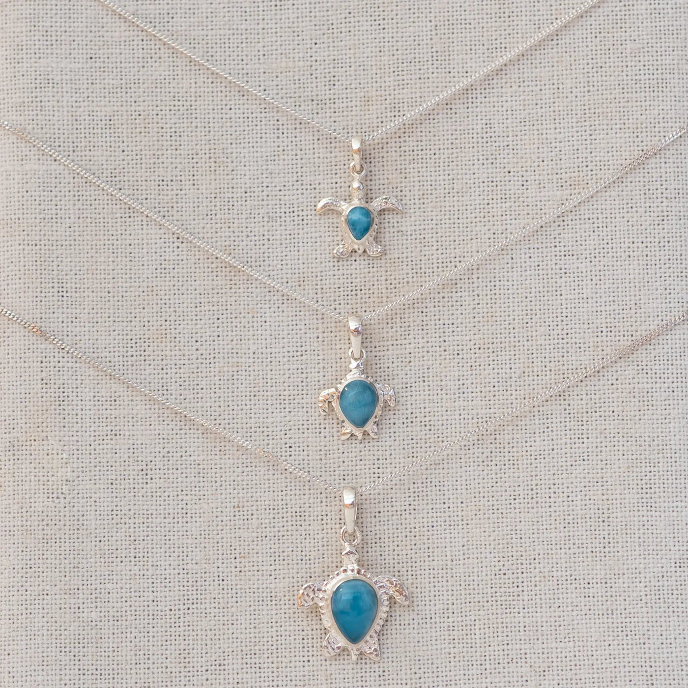 Trois bijoux tortues en argent 925 avec une pierre de larimar bleue au centre de chacune. Les trois tortues sont de dimensions différentes et attachées à une chaine en argent 925.