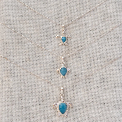 Trois bijoux tortues en argent 925 avec une pierre de larimar bleue au centre de chacune. Les trois tortues sont de dimensions différentes et attachées à une chaine en argent 925.