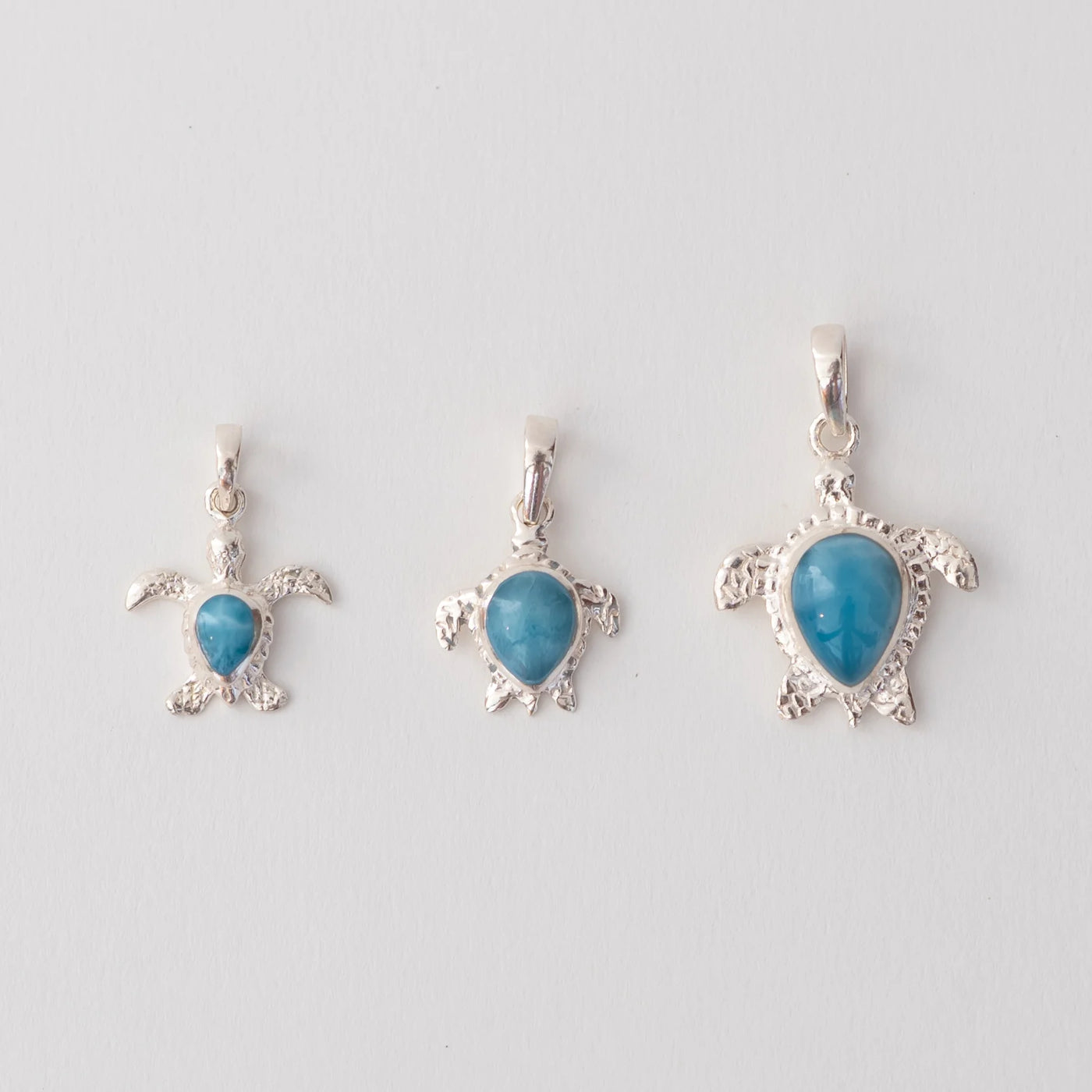 Trois bijoux en forme de tortues, faite en argent 925, avec sur chacune une pierre de larimar de République Dominicaine de couleur bleue. La pierr de larimar sur chaque tortue à une forme de goutte inversée.