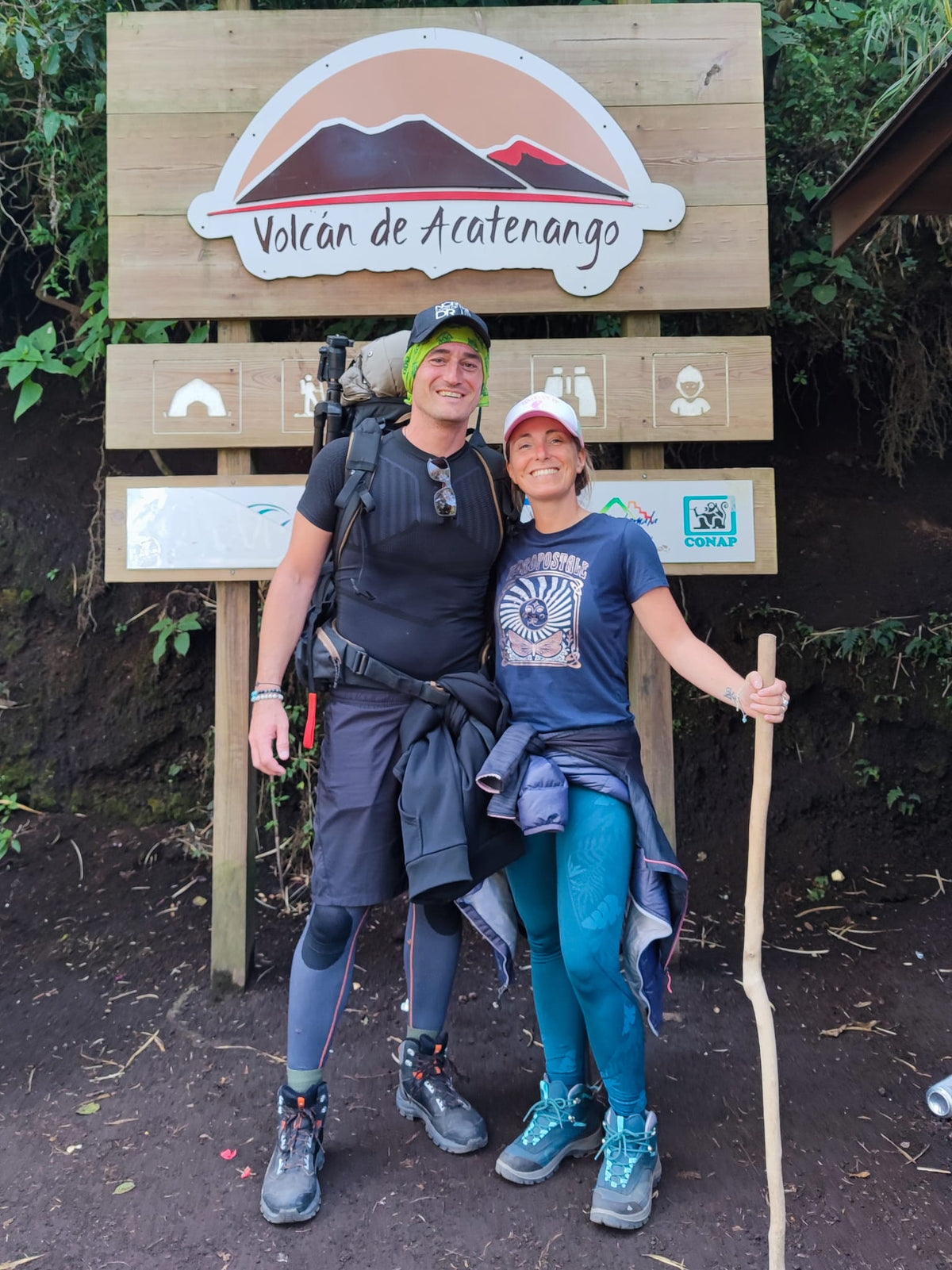 Jeune couple pris en photo devant la pancarte indiquant le sentier de l’ascension du volcan Acatenango. 