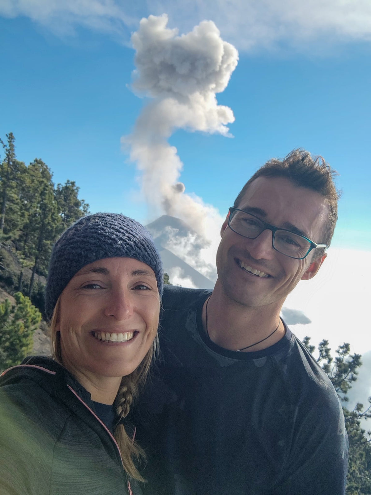 Couple français pris en photo selfie depuis le volcan Acatenango avec en fond le volcan El Fuego en éruption. Belle journée avec un ciel bleu.
