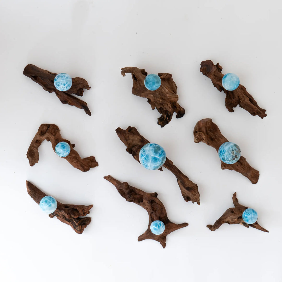 9 sphères taillées en Larimar de République Dominicaine sont vues de dessus et posées sur leur présentoir en bois. Chaque présentoir et chaque sphères sont uniques. Le Larimar est une pierre naturelle de couleur bleue.