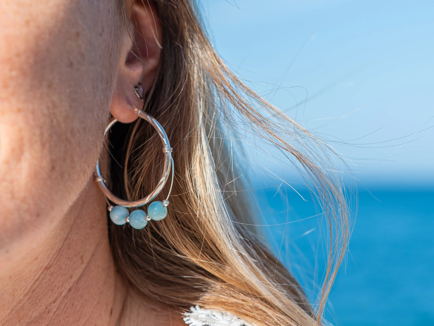 Vue proche de l'oreille d'une femme avec une boucle d'oreille en argent 925 en forme de créole et ses trois perles de larimar de République Dominicaine.
