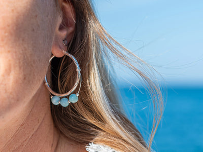 Vue proche de l'oreille d'une femme avec une boucle d'oreille en argent 925 en forme de créole et ses trois perles de larimar de République Dominicaine.