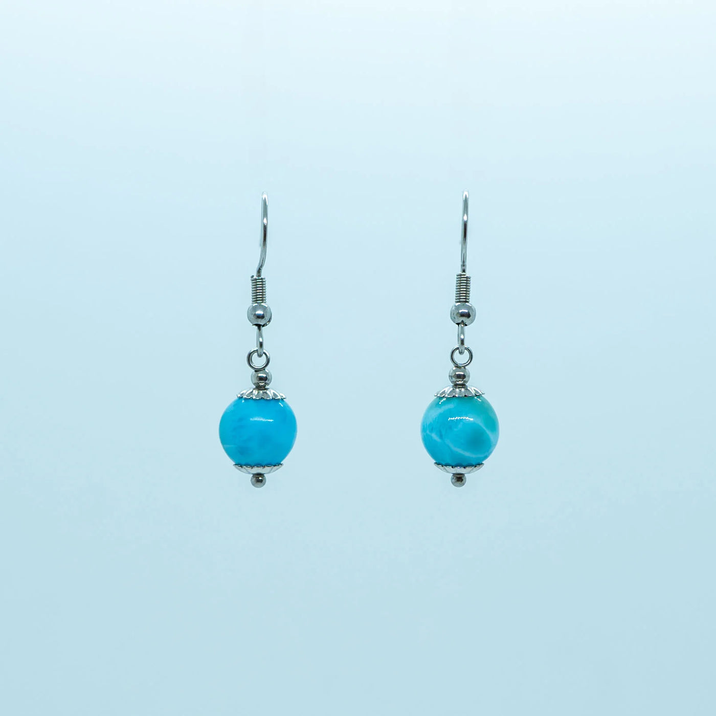 Paire de boucles d'oreilles en acier inoxydable 316L de couleur argentée, vue de face sur fond blanc. Une perle de larimar de République Dominicaine avec deux coupelles montée en pendant sur chaque boucle.