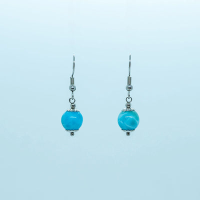 Paire de boucles d'oreilles en acier inoxydable 316L de couleur argentée, vue de face sur fond blanc. Une perle de larimar de République Dominicaine avec deux coupelles montée en pendant sur chaque boucle.